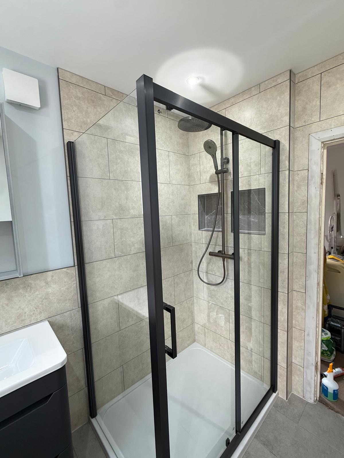 Black framed sliding shower enclosure with stone-effect tiling and recessed shelves