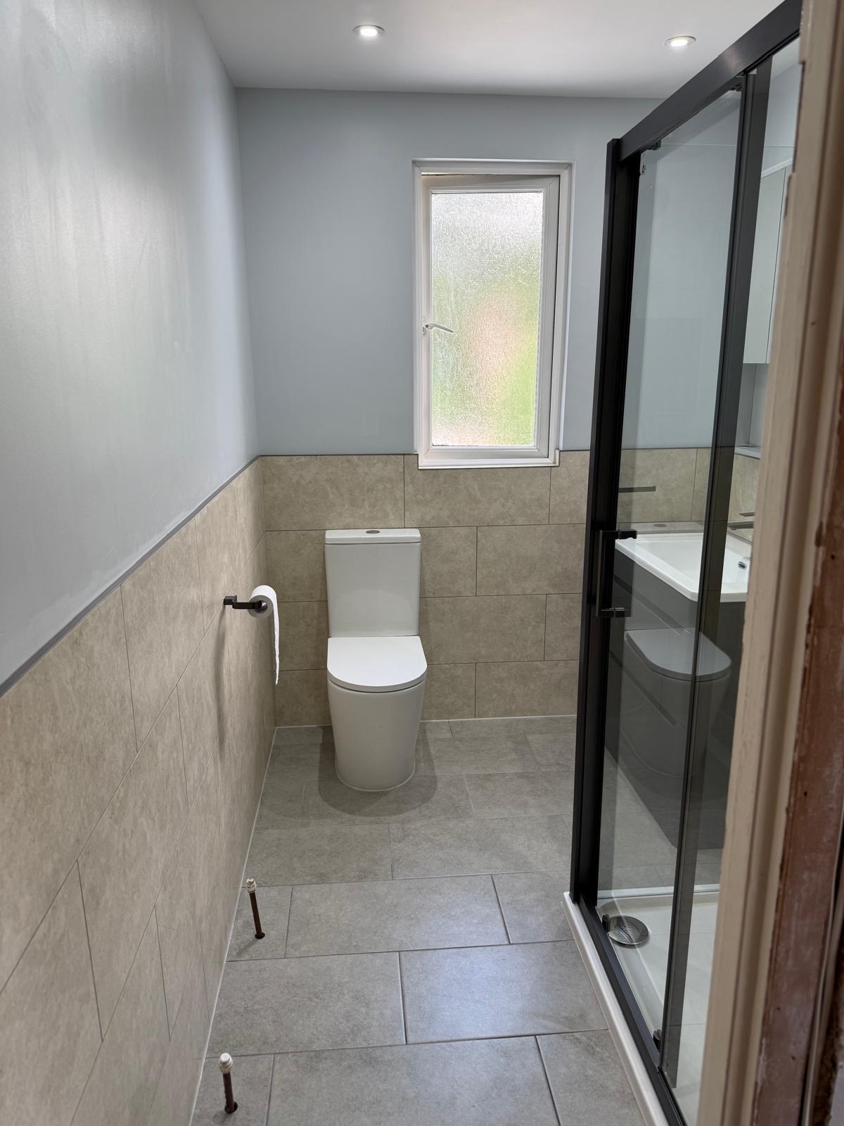 Shower room with half-tiled walls, close coupled toilet and black framed shower door