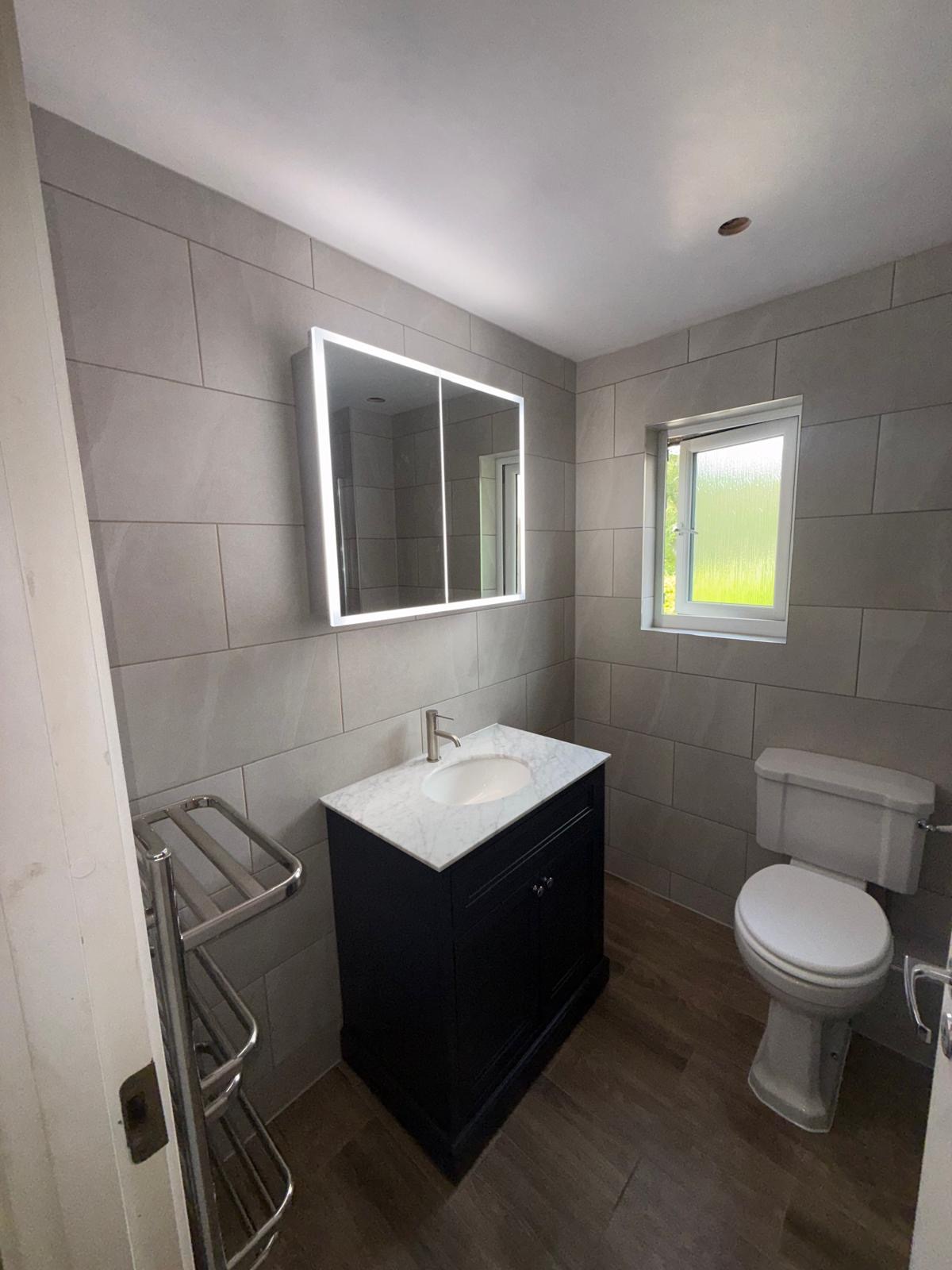 Bathroom with black vanity unit, marble top and LED mirror cabinet