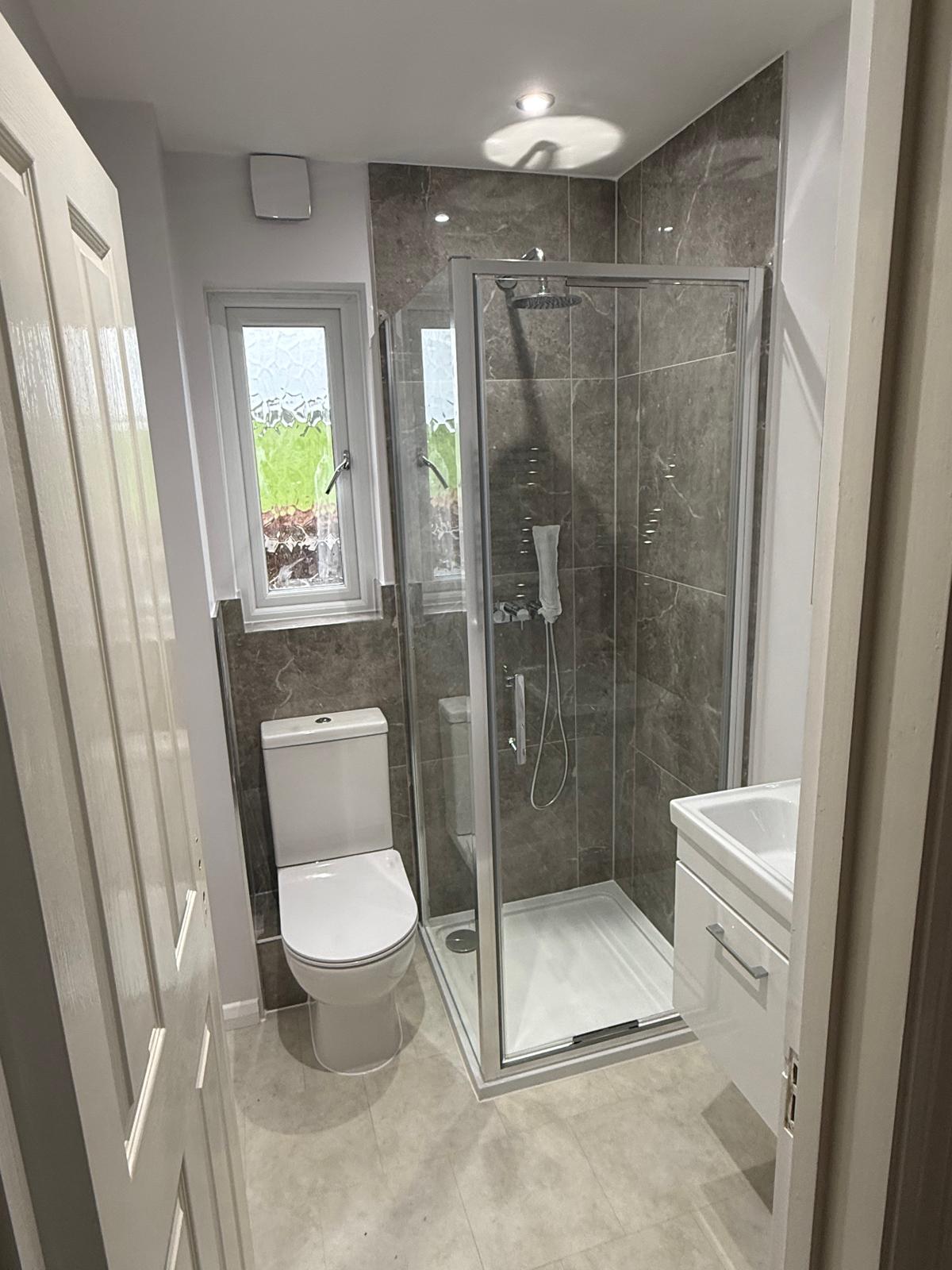 Compact shower room with dark marble-effect tiling and chrome shower enclosure