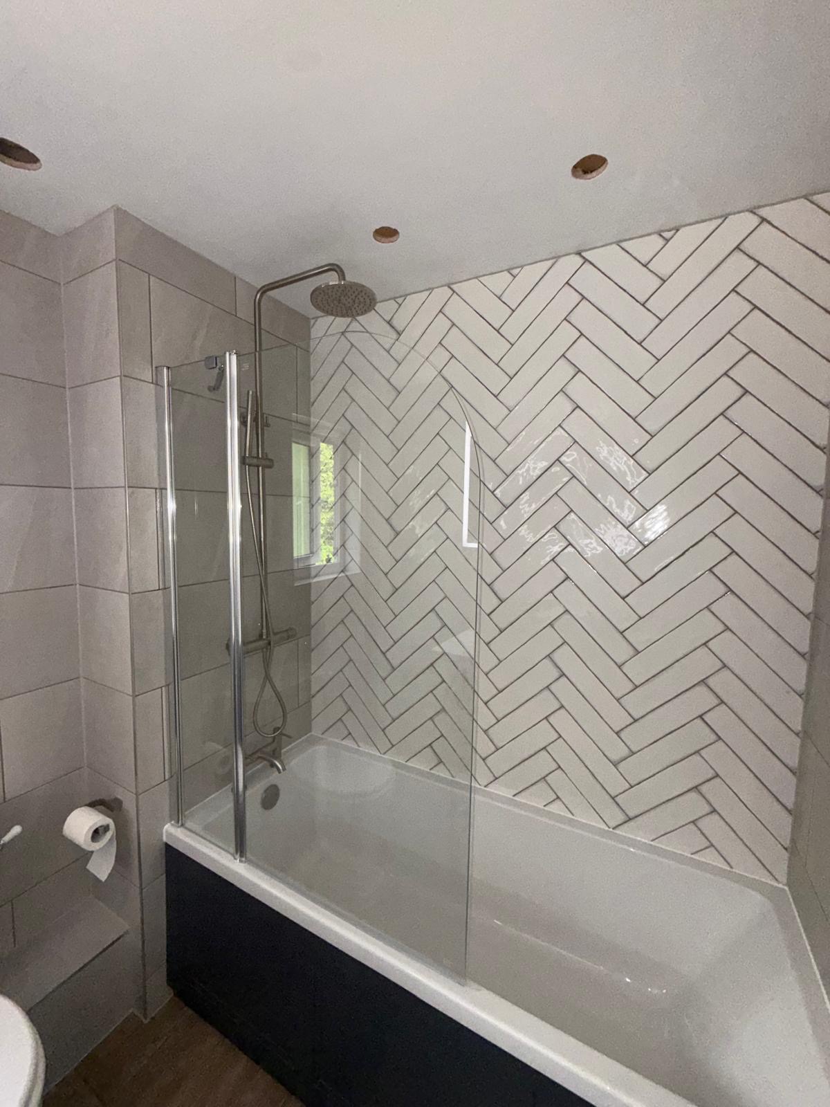 Bath with glass shower screen and white herringbone tiled wall, completed in Egham, Surrey