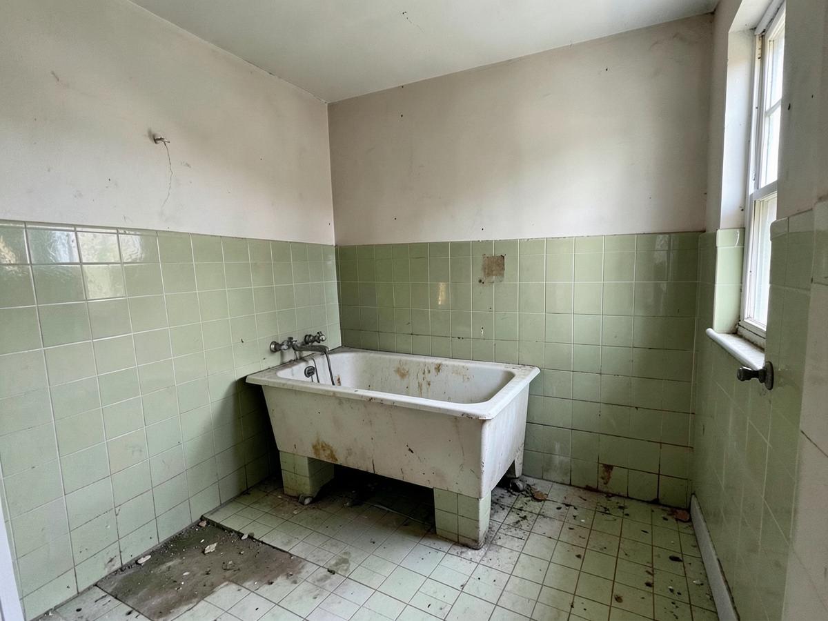 Dated bathroom with old green tiles and a worn bath before renovation