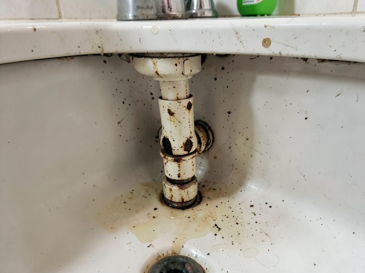 Corroded leaking waste pipe under a basin before repair